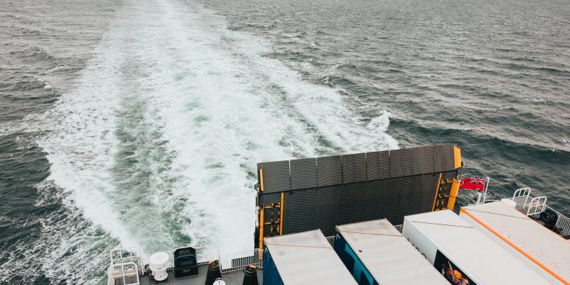 Manxman at sea, looking down on the quarterdeck from the starboard side of deck seven. freight trailers are visible on the exposed area of the vehicle deck. A white wake stretches out from the rear of the vessel towards the horizon