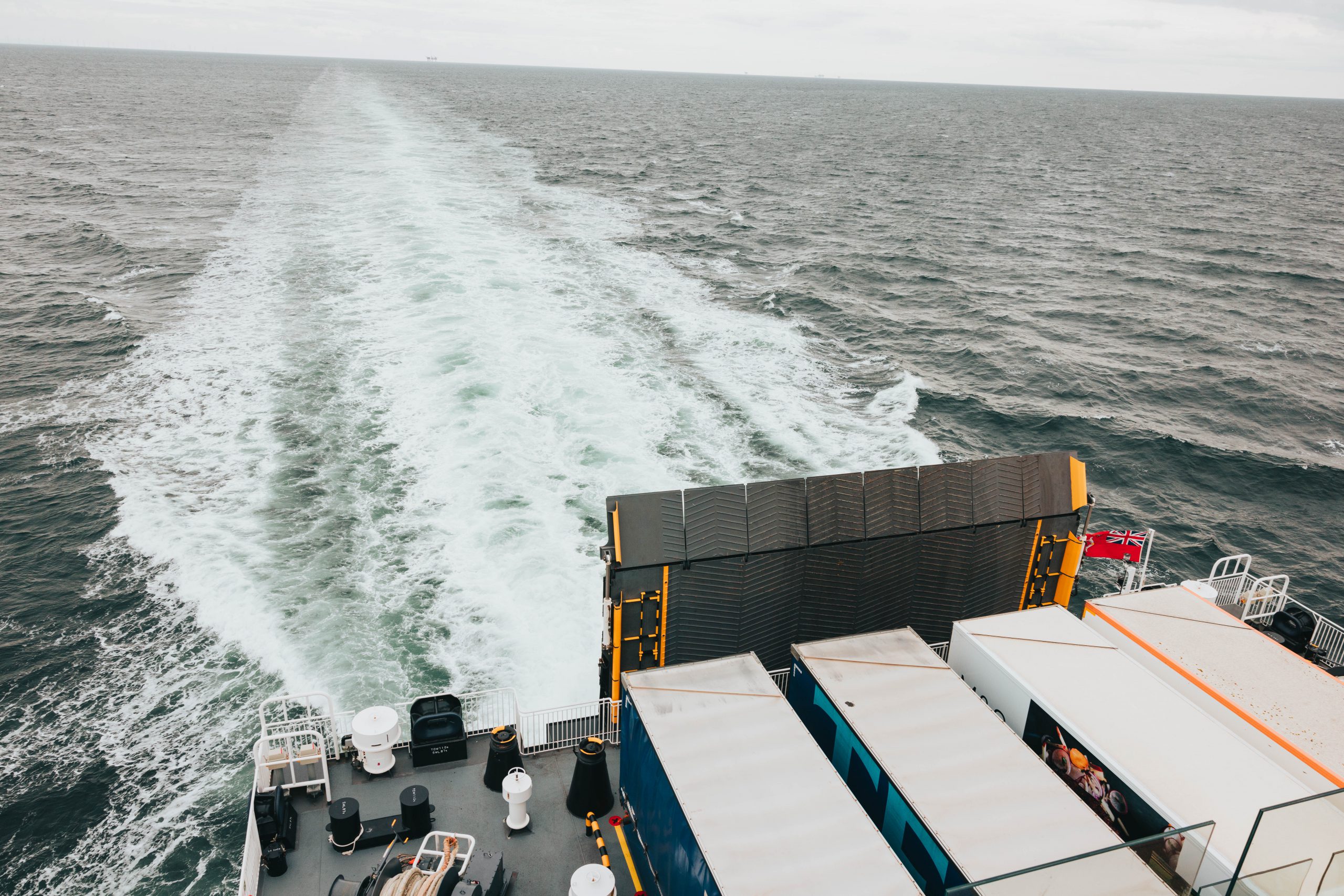 Manxman at sea, looking down on the quarterdeck from the starboard side of deck seven. freight trailers are visible on the exposed area of the vehicle deck. A white wake stretches out from the rear of the vessel towards the horizon