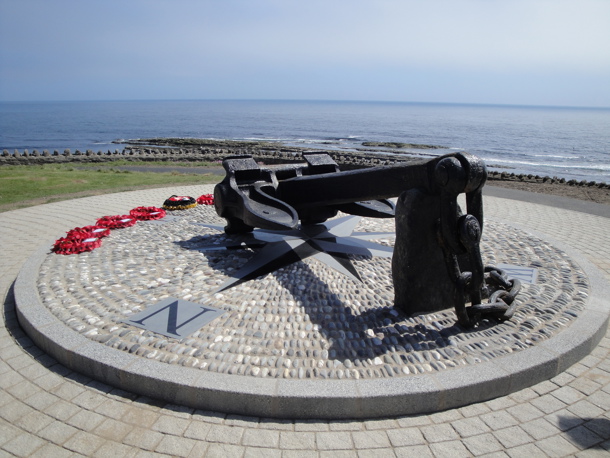 The memorial anchor of Mona’s Queen at Kallow Point in Port St Mary on a sunny day, with red wreaths lay on the ground