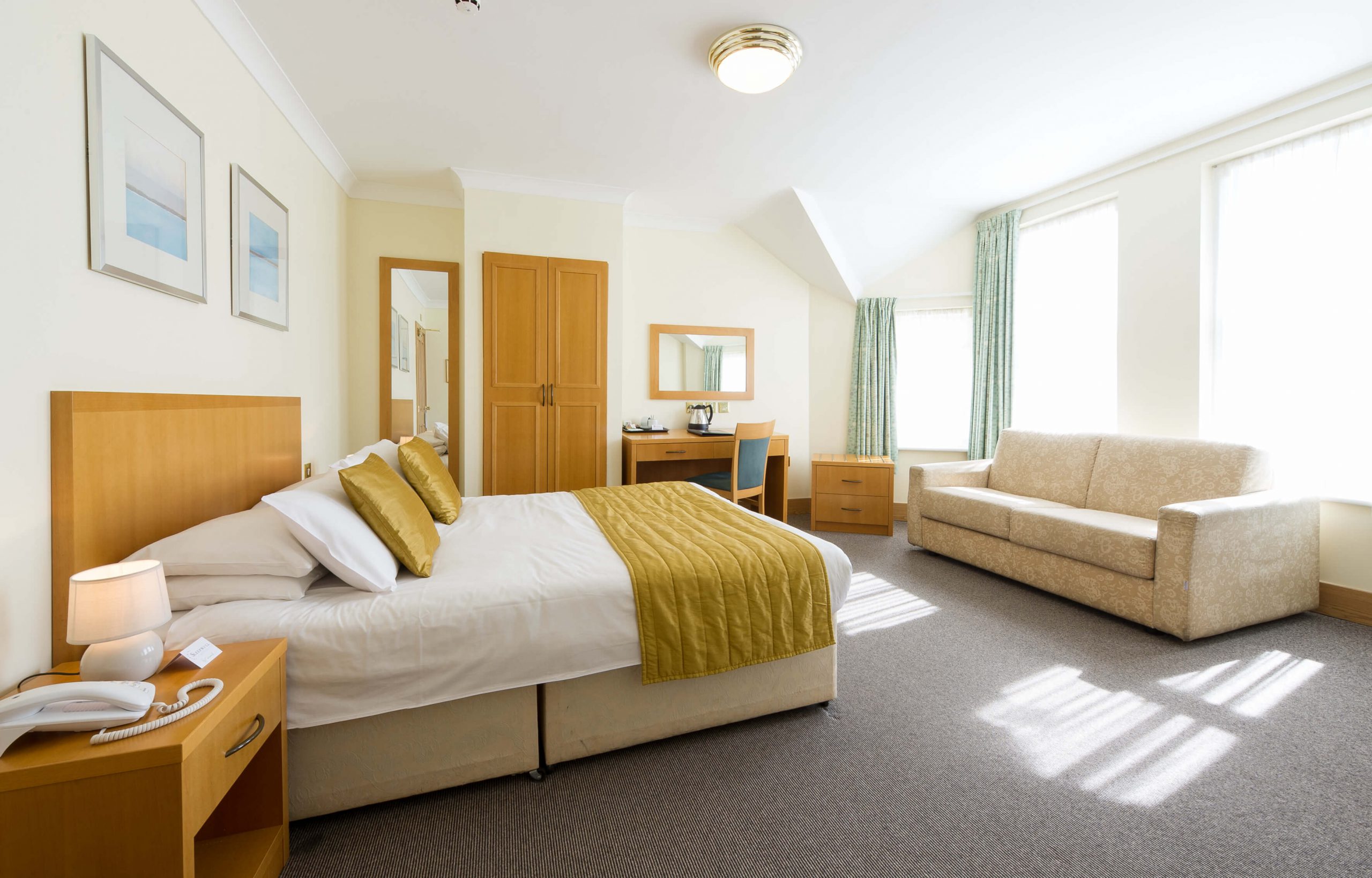 Large hotel bedroom with bed, soda and desk and windows