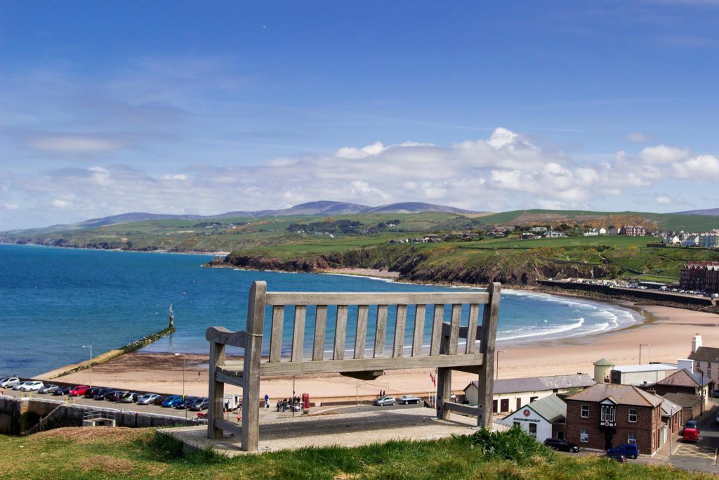 A bench on a hill looking out over Port Erin beach and coastline on a summers day