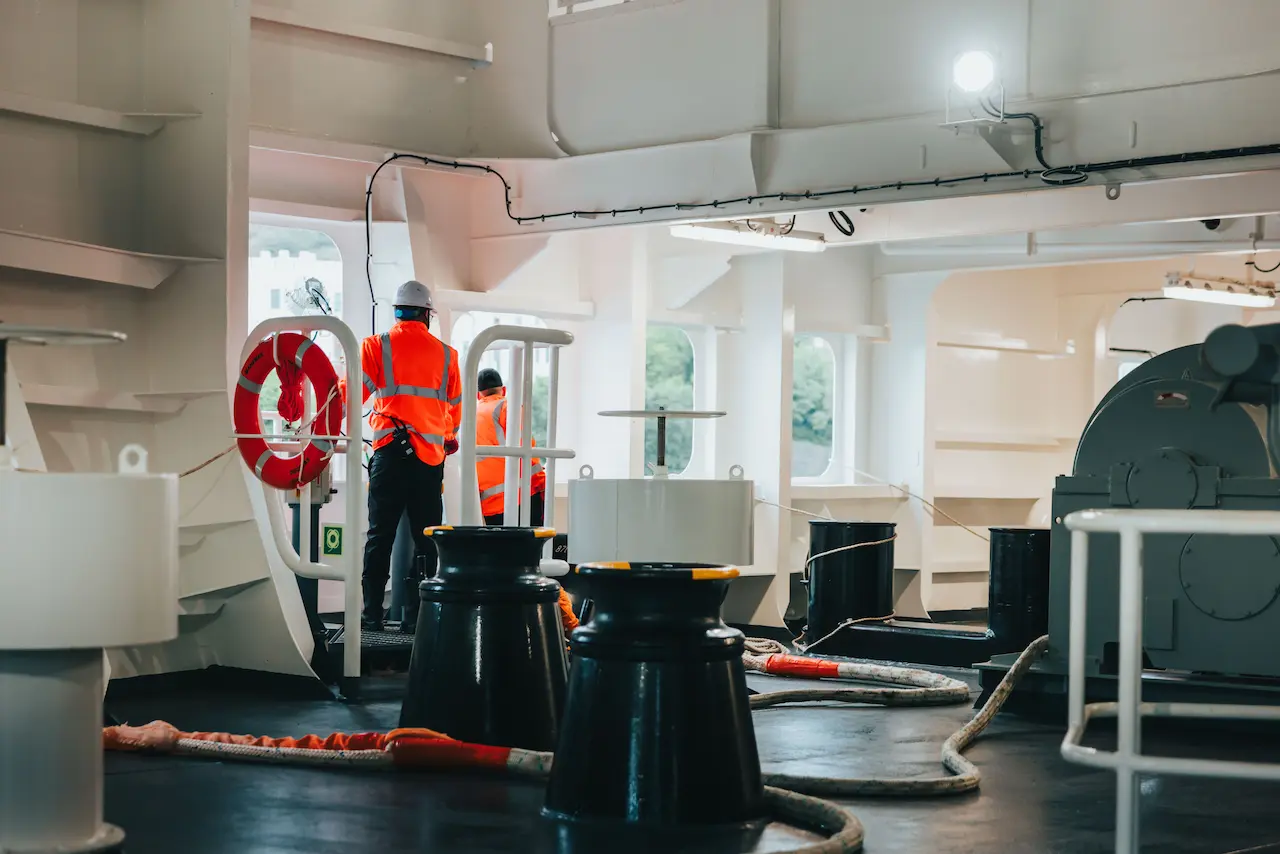 Crewmembers in the forward rope handling area of Manxman prepare to undertake berthing operations. in the foreground a number of bollards and winches are visible, with mooring lines snaking across the deck ready to be paid out. 