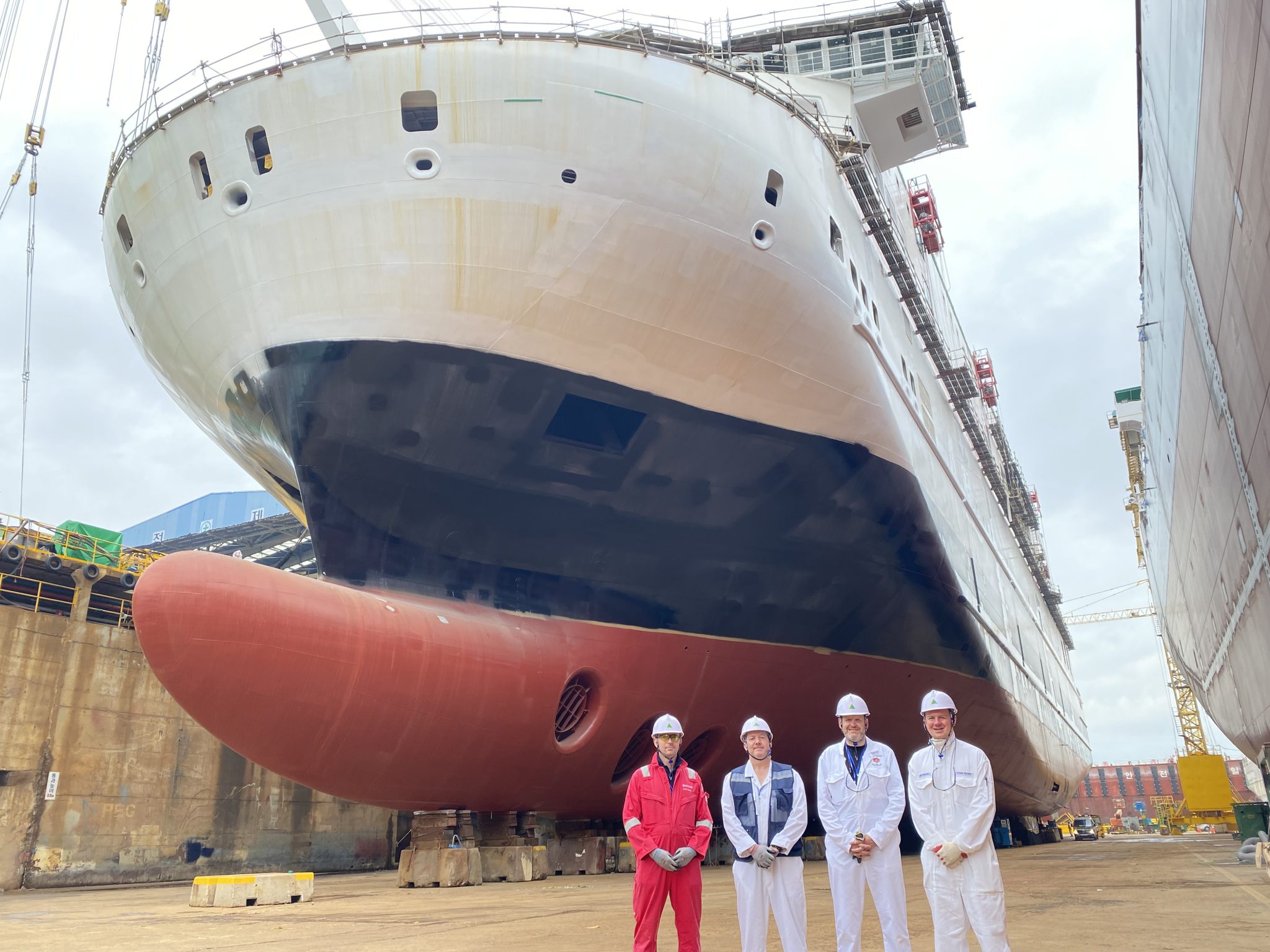 View of ferry in shipyard looking up at the ferry with 4 team members standing in front