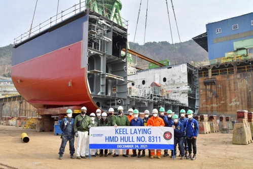 Section of a ferry in shipyard being built with team who helped build it standing in front and holding banner saying "Keel Laying HMD Hull No.8311, December 24, 2021”